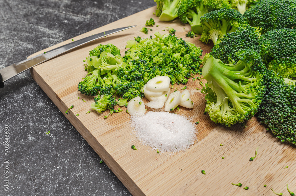 Green broccoli vegetable with garlic and salt on wooden board. Sharp kitchen knife. Dark background. Green broccoli vegetable with garlic and salt on wooden board. Sharp kitchen knife. Dark background.