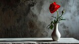 A smooth, matte surface holds a slender vase with a single, blooming red rose. 