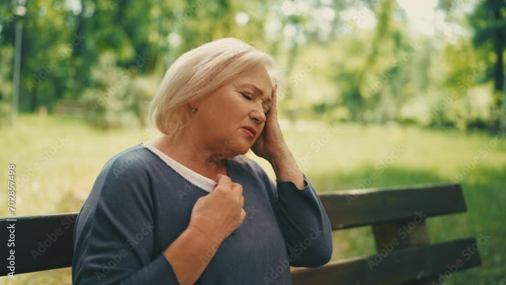 Senior female having headache and hot flush, sitting on bench in summer park Senior female having headache and hot flush, sitting on bench in summer park