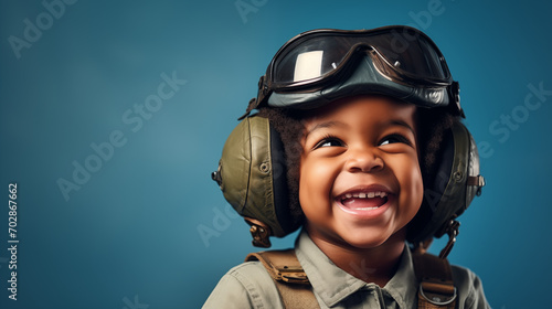 A cute black kid dressed as a pilot smiling at the camera on a plain blue background photo