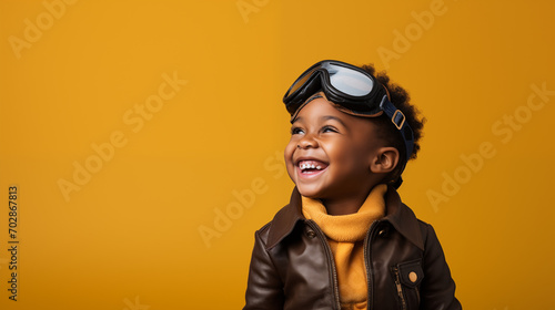 A cute black kid dressed as a pilot smiling at the camera on a plain yellow background photo