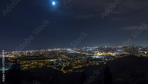 Night Timelapse of Barcelona and Badalona Skylines. Aerial View from Iberic Puig Castellar Village Viewpoint, Illuminating Roofs of Houses and the Sea on the Horizon Under the Starry Night Sky photo