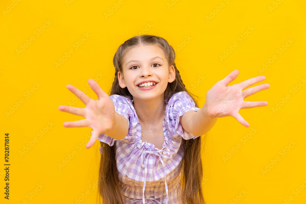 A beautiful little girl stretches her arms out, palms forward, and smiles broadly. A happy child. Yellow isolated background. A beautiful little girl stretches her arms out, palms forward, and smiles broadly. A happy child. Yellow isolated background.
