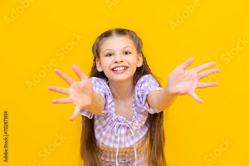 A beautiful little girl stretches her arms out, palms forward, and smiles broadly. A happy child. Yellow isolated background. photo