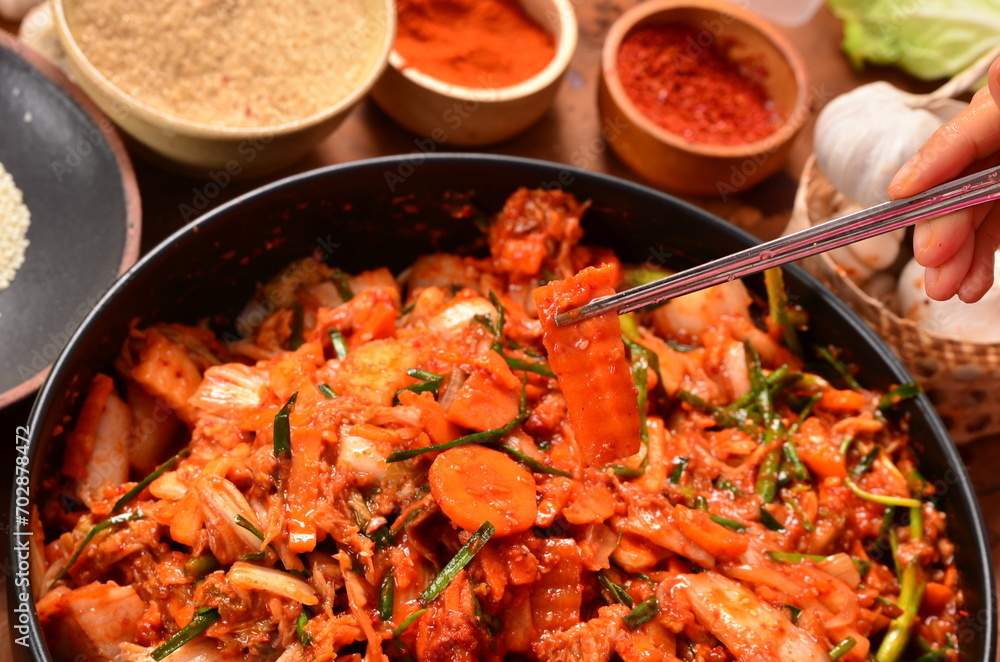 One person uses chopsticks to pick up kimchi onto a black ceramic blow. One person uses chopsticks to pick up kimchi onto a black ceramic blow.