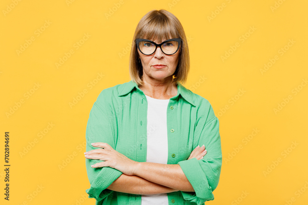Elderly sad frowning blonde woman 50s years old wears green shirt glasses casual clothes hold hands crossed folded look camera isolated on plain yellow background studio portrait. Lifestyle concept. - obrazy, fototapety, plakaty 