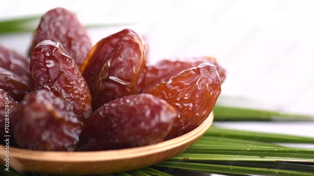 Dates fruit. Date fruits in wooden bowl with palm tree leaf isolated on white background. Medjool dates close up. Slow motion. 