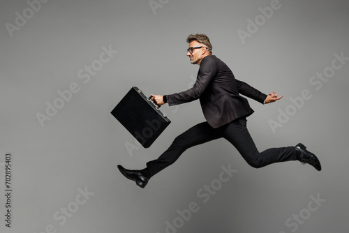 Full body adult successful employee business man corporate lawyer in classic formal black suit shirt tie work in office jump high hold briefcase run isolated on plain grey background studio portrait