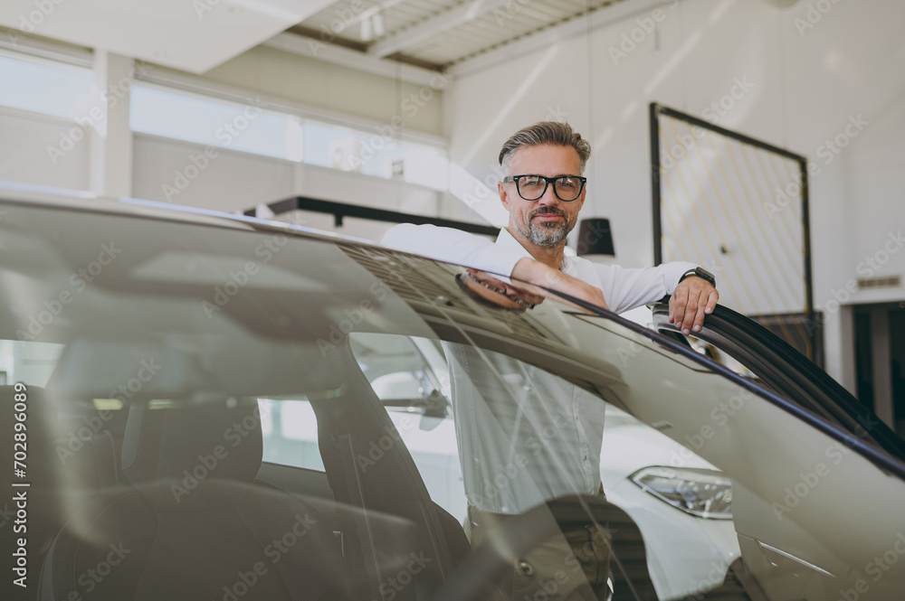 Adult fun man customer male buyer client wearing shirt glasses open door get into black car choose auto want to buy new automobile in showroom vehicle salon dealership store motor show. Sales concept. Adult fun man customer male buyer client wearing shirt glasses open door get into black car choose auto want to buy new automobile in showroom vehicle salon dealership store motor show. Sales concept.