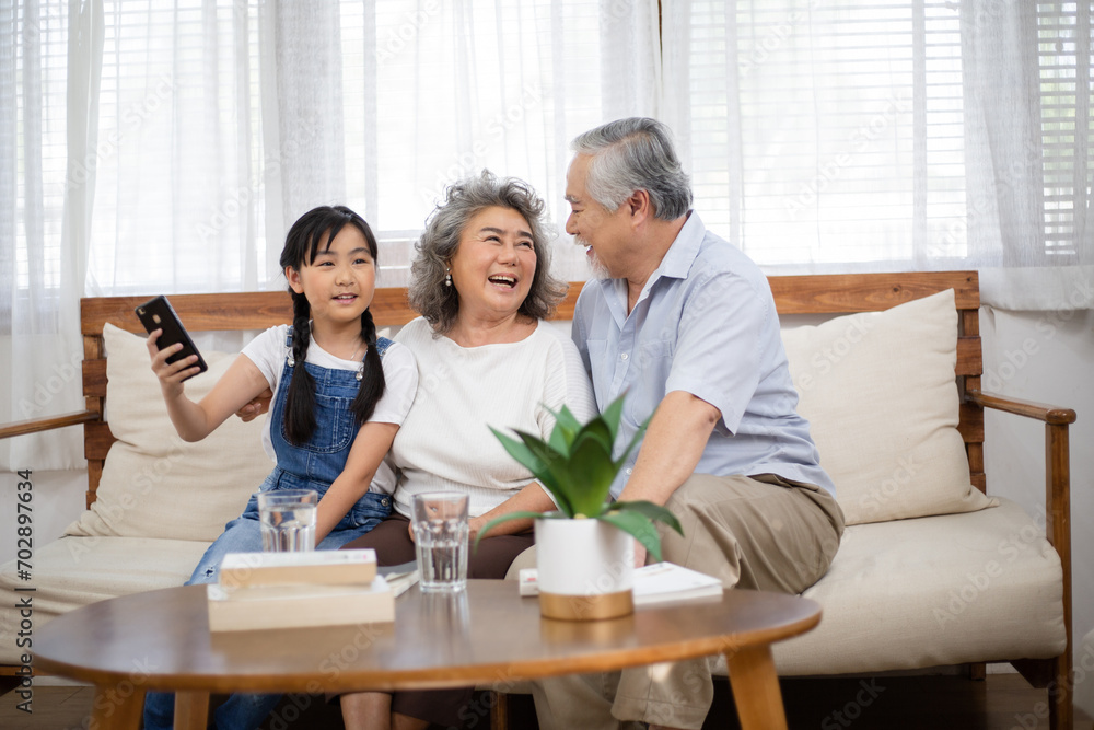 Asian senior couple enjoy talking with granddaughter in the living room. Little girl visit her grandparents at home on holidays weekend. Love and bonding family spending time together. Asian senior couple enjoy talking with granddaughter in the living room. Little girl visit her grandparents at home on holidays weekend. Love and bonding family spending time together.
