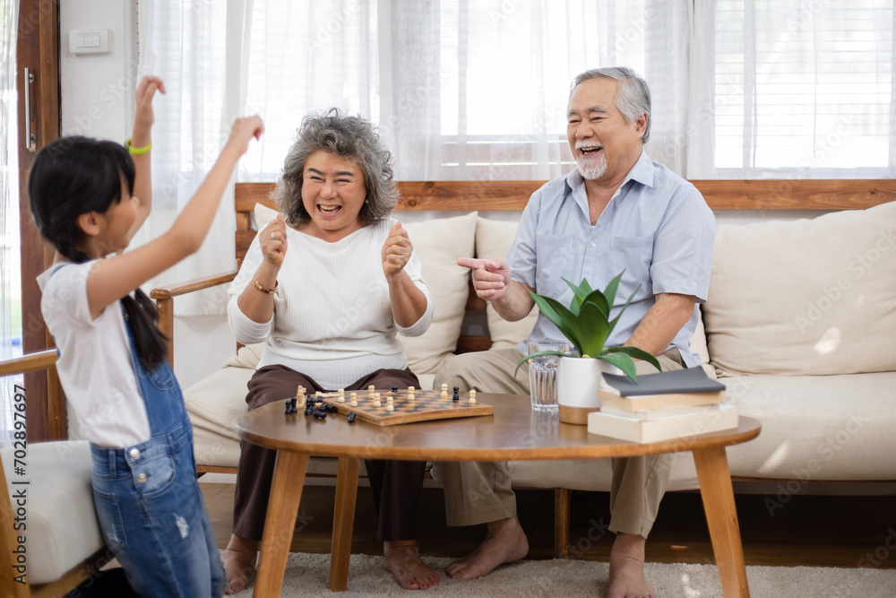Asian girl playing chess with grandparents and win the game. Senior couple support and cheer up granddaughter. Happy family smiling and laughing together. Healthy living insurance Asian girl playing chess with grandparents and win the game. Senior couple support and cheer up granddaughter. Happy family smiling and laughing together. Healthy living insurance