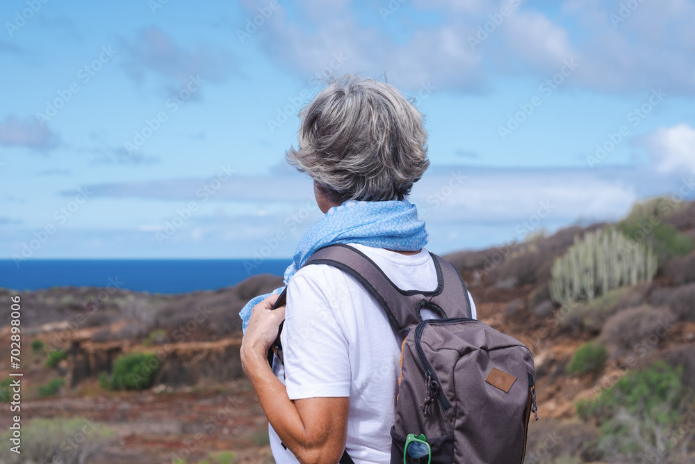 Back view of senior woman carrying backpack in outdoor excursion enjoying sunny day, freedom and sea vacation. Healthy lifestyle and happy retirement concept Back view of senior woman carrying backpack in outdoor excursion enjoying sunny day, freedom and sea vacation. Healthy lifestyle and happy retirement concept