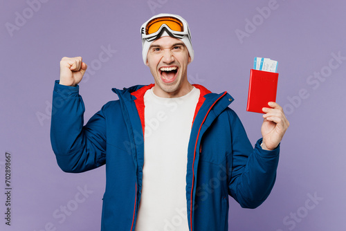 Traveler winner skier man in blue windbreaker jacket ski goggles mask hold passport ticket isolated on plain purple background Tourist travel abroad in free time rest getaway Air flight trip concept