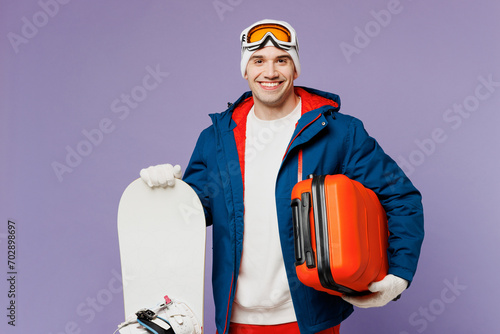 Traveler happy man wear blue windbreaker jacket ski goggles mask hold snowboard bag isolated on plain purple background. Tourist travel abroad in free spare time rest getaway. Air flight trip concept. #702898697