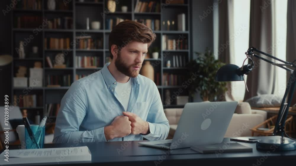 young man sits at table working at laptop in home office. waits nervously looking at screen without blinking. gets great news and is delighted. waves and claps hands, laughs, exclaims yes. leans back young man sits at table working at laptop in home office. waits nervously looking at screen without blinking. gets great news and is delighted. waves and claps hands, laughs, exclaims yes. leans back