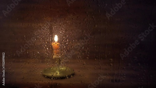 burning old candle with vintage brass candlestick in window with drops are running down glass, concept cozy warm home in rainy weather
