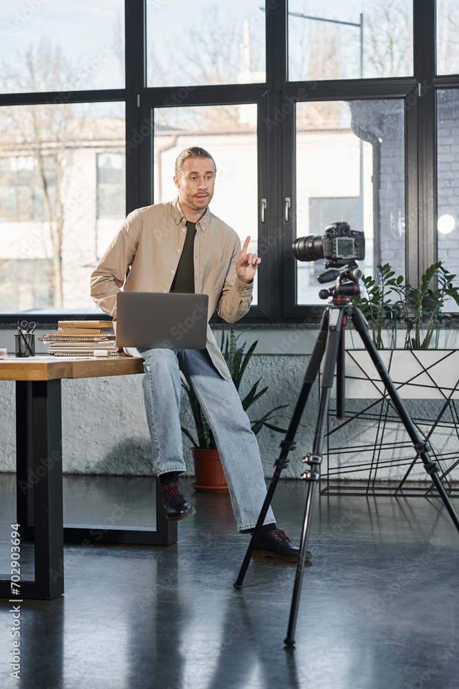 businessman sitting on work desk with laptop and talking in front of digital camera, video blog