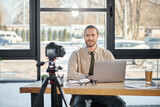 successful entrepreneur sitting at work desk in front of digital camera during video blog in office