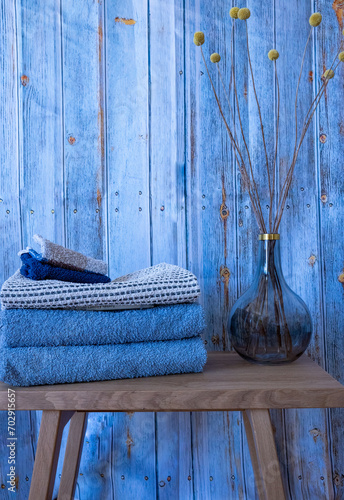 In the bathroom.  Wooden stool with blue and white towels and washcloths on it.  Blue retro background and decorative vase with Craspedia globosa photo