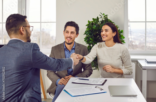 Portrait of a happy couple shaking hands with a male business broker, realtor or insurance agent. Cheerful young man and woman having a good deal with their investment adviser sitting in the office. photo