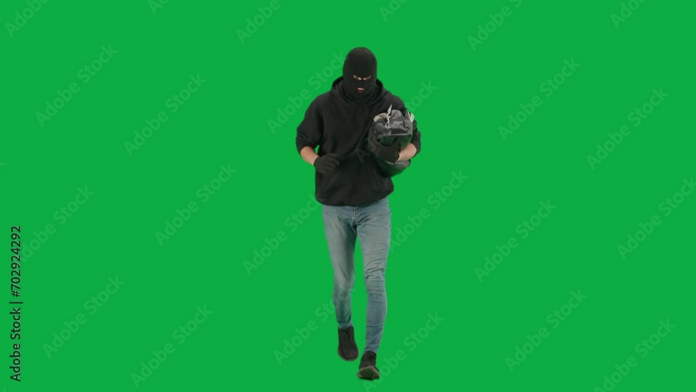 Portrait of thief on chroma key green screen background. Man robber wearing hoodie, jeans and balaclava, running from police with stolen bag full of money. Portrait of thief on chroma key green screen background. Man robber wearing hoodie, jeans and balaclava, running from police with stolen bag full of money.