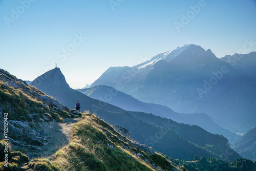 Young sporty female hiker on idyllic trail in awesome dolomite mountain landscape. View to iconic Marmolada summit. Hiking near Gardena Valley in South Tyrol, Italy #702929442