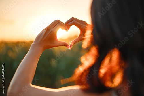 Young woman making heart shape with her hands at sunset, Love sign.