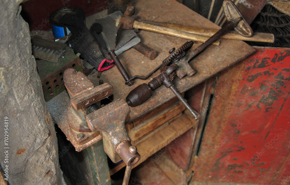 Workplace of a foreman in an old workshop. old bench vice and hand drill. old tools on a dark photo. Workplace of a foreman in an old workshop. old bench vice and hand drill. old tools on a dark photo.