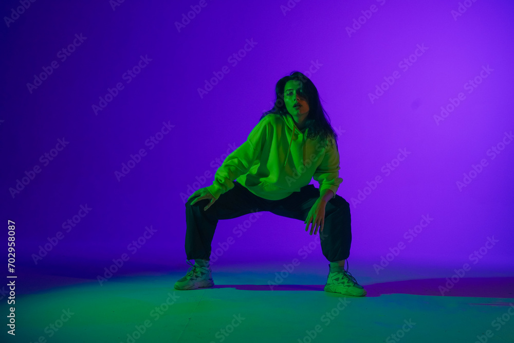 Live jazz-funk performance in the studio: a young stylish girl in casual clothes embodies the rhythm and energy of dance under purple-green light.