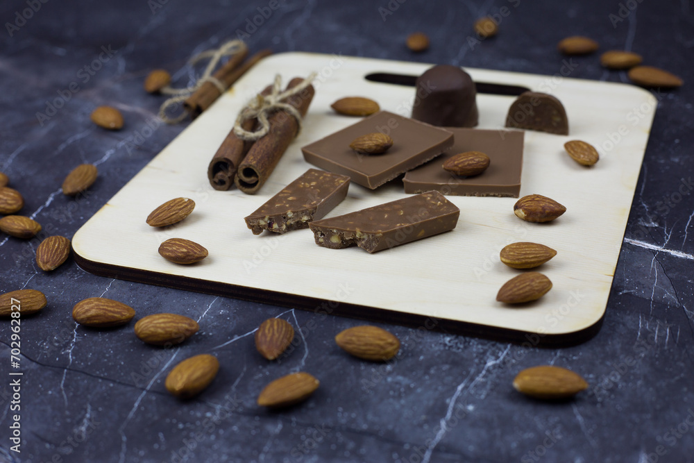 Chocolate set for serving on a wooden board on a dark table. Sweet dish of chocolate bars and candies with almonds Chocolate set for serving on a wooden board on a dark table. Sweet dish of chocolate bars and candies with almonds