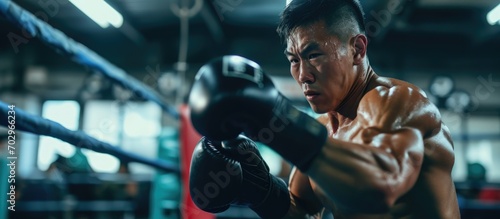 Asian fitness trainer supports athlete in boxing gym.