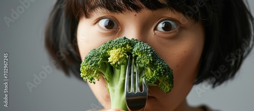 Asian women reluctantly observe broccoli on a fork during mealtime, expressing dislike for vegetables. photo
