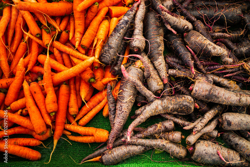A pile of freshly harvested orange and purple carrots in open shade at a farmers market in California photo