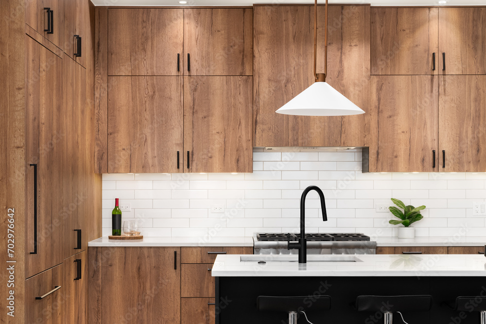 A kitchen detail with wood cabinets, a black faucet, subway tile backsplash, and gold light fixtures hanging above the black island and marble countertops. - obrazy, fototapety, plakaty 