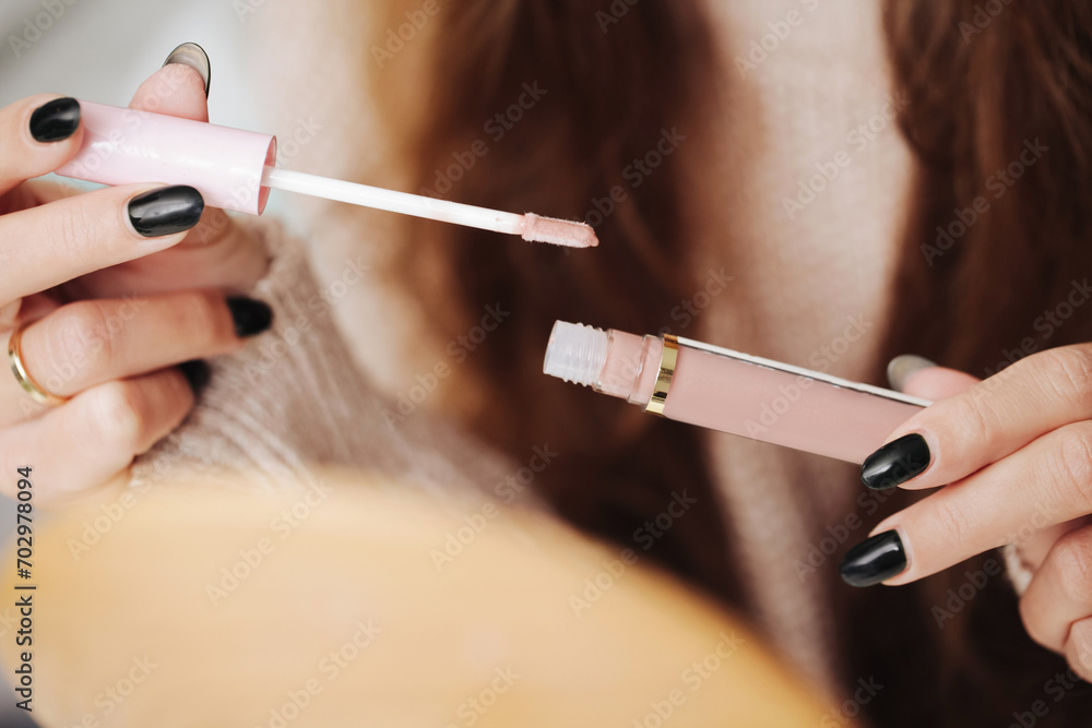 Long haired woman opening lip gloss. Cosmetics background. Pink lips. Girl doing makeup in front of a mirror. Closeup on product container in tube. Long haired woman opening lip gloss. Cosmetics background. Pink lips. Girl doing makeup in front of a mirror. Closeup on product container in tube.