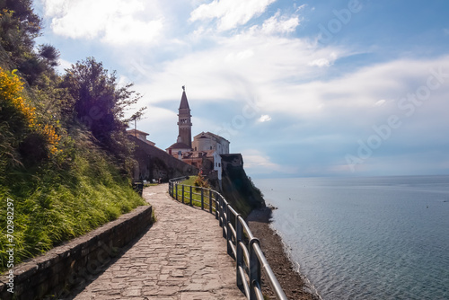 Scenic walking path between Fiesa and charming coastal town of Piran, Slovenian Istria, Slovenia, Europe. Panoramic view of St George Parish Church. Shimmering waters of the Adriatic Mediterranean Sea