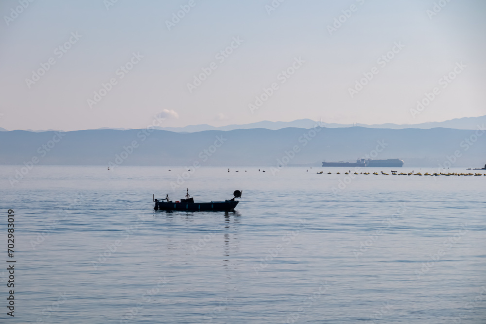Fishing boat with panoramic view of idyllic coastline seen from Gulf of Piran, Adriatic Mediterranean Sea, Slovenia, Europe. Summer seaside vacation. Distant mountain ranges of Julian Alps