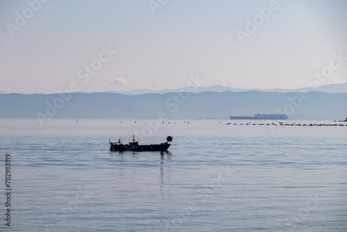 Fishing boat with panoramic view of idyllic coastline seen from Gulf of Piran, Adriatic Mediterranean Sea, Slovenia, Europe. Summer seaside vacation. Distant mountain ranges of Julian Alps © Chris