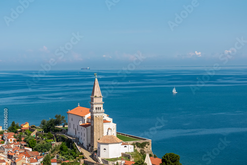 Saint George Parish Church with panoramic aerial view of coastal town Piran, Primorska, Slovenia, Europe. Looking from town walls Shimmering azure waters of Adriatic Sea. Mediterranean architecture
