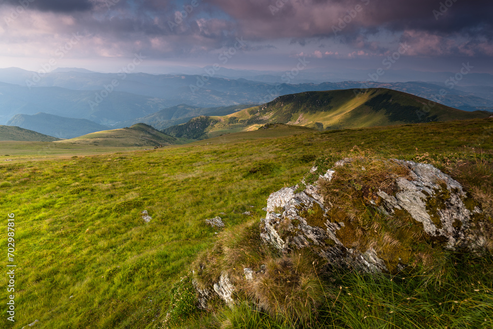 Wonderful springtime panoramic landscape in mountains at sunset. Grassy slopes and forested hills illuminated with morning sunshine.