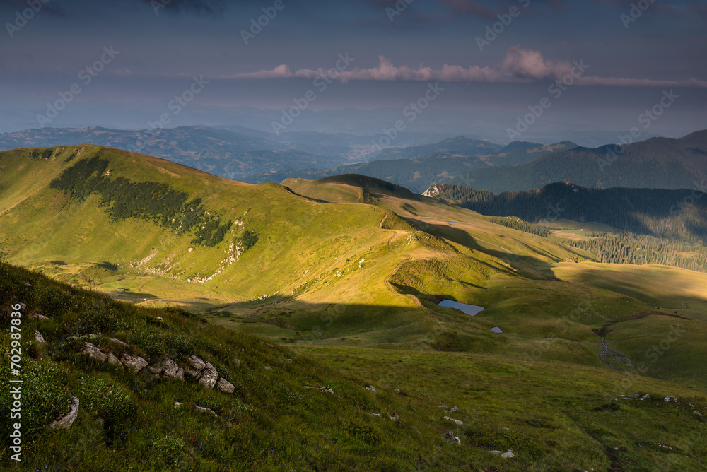 Wonderful springtime panoramic landscape in mountains at sunset. Grassy slopes and forested hills illuminated with morning sunshine.