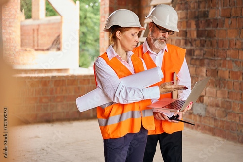 Construction professionals analyzing data on computer in uncompleted house