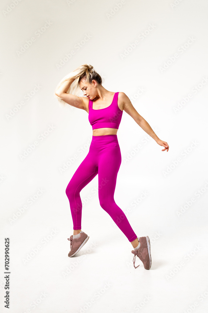 Woman in vibrant pink sports outfit on toes holding hairs with one hand