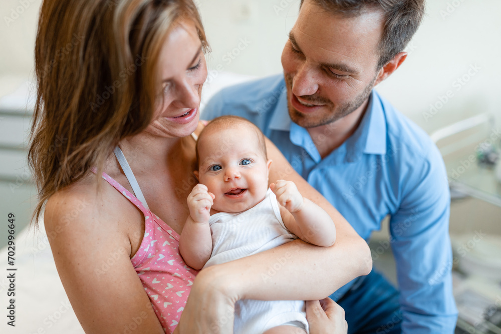 Happy smiling mother and father holding their newborn baby in hospital room. Newborn baby with blue eyes looking at camera. Happy smiling mother and father holding their newborn baby in hospital room. Newborn baby with blue eyes looking at camera.