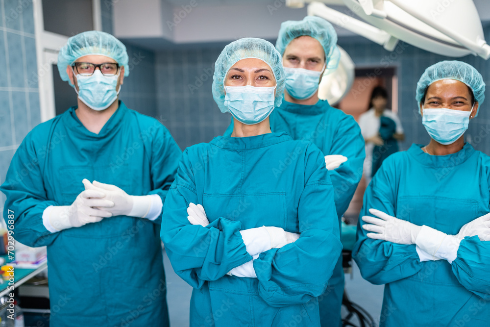 Medical team of confident successful surgeons in operating room standing with arms crossed and looking at camera as they pose together for a portrait, dressed professionally in operating gowns. Medical team of confident successful surgeons in operating room standing with arms crossed and looking at camera as they pose together for a portrait, dressed professionally in operating gowns.