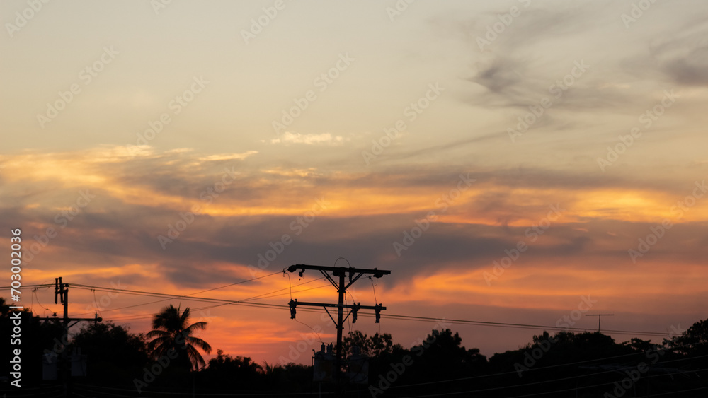 Sunset sky with silhouette of coconut tree and electricity post on the road.