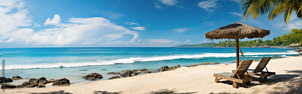 Panoramic view of beautiful tropical beach with white sand, turquoise water, palm trees and sun loungers.