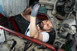 Focused automotive service technician is fixing automobile in inspection pit