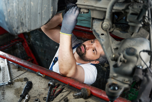 Focused automotive service technician is fixing automobile in inspection pit