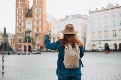 Attractive female tourist is exploring new city. Redhead woman pointing finger on Market Square in Krakow. Traveling Europe in autumn. St. Marys Basilica. Active lifestyle